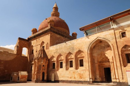 Ottoman tomb next to a row of barred windows and a gate with the mosque with its red cupola, dome in the background, in the second court inside the Ishak Pasha Palace, Sarayi, Dogubeyazit, Turkey 2022