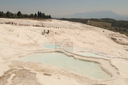 A crowd of people climbing up the travertine pools in Pamukkale from the lower gate on a busy day, Denizli, Turkey 2022