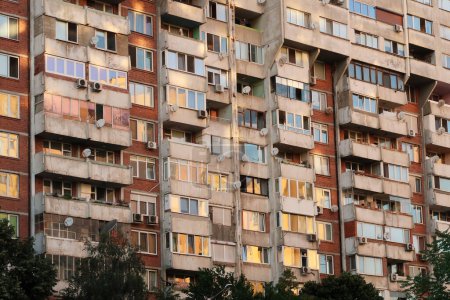 Les nombreuses fenêtres d'un panneau de béton, socialiste, brutaliste, multi-étages, gratte-ciel, immeuble, reflètent le coucher de soleil en orange, jaune, rose, Sofia, Bulgarie 2022