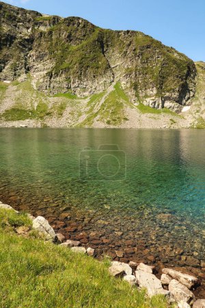 The mountains are reflecting in the blue, green, turquoise water of the Kidney, Babreka Lake, one of the Seven Rila Lakes, situated on a plateau in the Rila National Park, close to Sofia, Bulgaria 2022