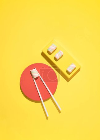 Foto de Colourful marshmallow candies served as sushi with chopsticks on yellow background. Flat lay. - Imagen libre de derechos