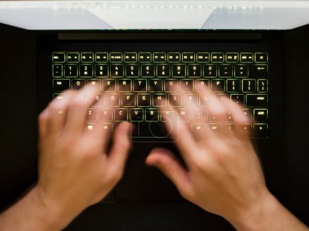 Foto de Desenfoque Manos de velocidad escribiendo en un teclado verde retroiluminado de un ordenador portátil - Imagen libre de derechos