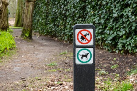 Foto de Señalización con pictogramas para perros prohibidos defecar y perros deben estar atados en el sendero en el bosque, Hilversum, Países Bajos - Imagen libre de derechos