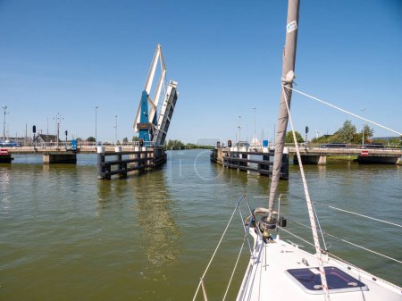 Photo for WARNS, NETHERLANDS - JUL 7, 2023: Sailboat approaching bridge waiting for opening - 3/4, Warnsebrug bridge over Johan Frisokanaal channel in Friesland, Netherlands - Royalty Free Image