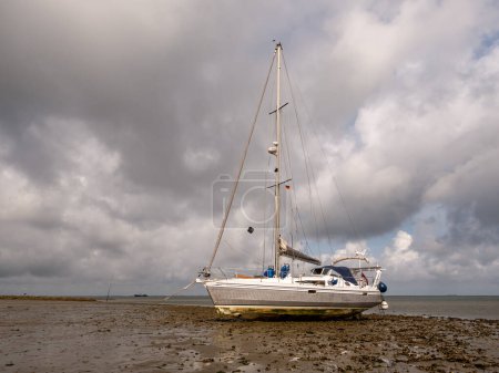 Sailboat dried out aground on mud flat at low tide of Wadden Sea east of Hooge Hallig, North Frisia, Schleswig-Holstein, Germany