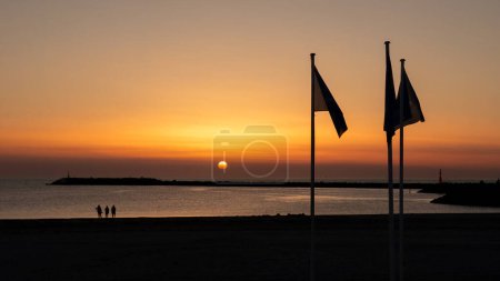 People on beach watching sunset over North Sea and South Pier of Hvide Sande harbour, Central Jutland, Denmark