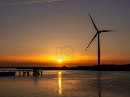 Hvide Sande channel with wind generator and jetty at sunset over North Sea, Central Jutland, Denmark