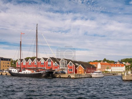 Téléchargez les photos : Hadsund, Danemark - Sep 21, 2023 : Voilier et immeuble de bureaux de couleur rouge le long du Mariagerfjord, Hadsund, Himmerland, Nordjylland, Danemark - en image libre de droit