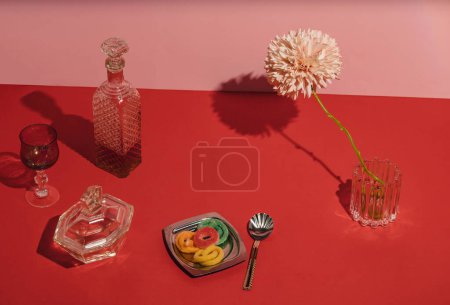 Foto de Red table for a party. Gummy candy, crystal bottle and glasses, teaspoon, pink flower and other things on the table.. - Imagen libre de derechos