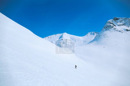 Téléchargez les photos : Plan grand ouvert de la figure solitaire de l'homme marcher sur la pente de la montagne lors d'une randonnée d'aventure en alpinisme ou d'une randonnée à ski. Activités hivernales en plein air en pleine nature - en image libre de droit