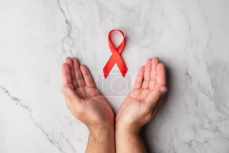 Téléchargez les photos : Les mains ouvertes d'un homme affichant un ruban rouge à l'appui de la Journée mondiale du sida. Comprendre avec les personnes infectées par le VIH - en image libre de droit