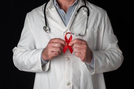 Téléchargez les photos : Docteur tient un ruban rouge avec les deux mains, symbole de la Journée mondiale du sida. Soutien du personnel de santé aux personnes atteintes du VIH. Prévention et lutte contre le virus du sida - en image libre de droit