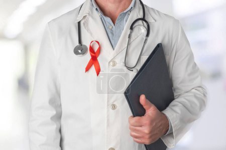 Téléchargez les photos : Docteur tenant un dossier avec des rapports médicaux et portant un ruban rouge sur sa poitrine, symbole de la Journée mondiale du sida. Soutien du personnel de santé aux personnes atteintes du VIH. Prévention et lutte contre le virus du sida - en image libre de droit
