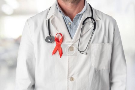 Téléchargez les photos : Docteur portant un ruban rouge sur sa poitrine, symbole de la Journée mondiale du sida. Soutien du personnel de santé aux personnes atteintes du VIH. Prévention et lutte contre le virus du sida - en image libre de droit