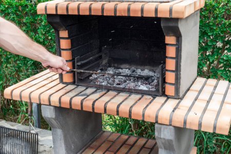 Foto de Hombre revolviendo las brasas de carbón en una barbacoa de ladrillo para asar carne - Imagen libre de derechos