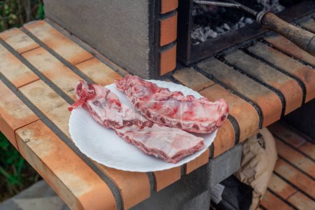 Foto de Placa de costillas de cerdo preparadas para asar en la barbacoa. Carne fresca lista para cocinar en la barbacoa de ladrillo del jardín - Imagen libre de derechos