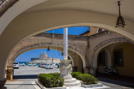 Téléchargez les photos : Rhodes, Grèce - 04 juillet 2021 : L'ancien palais du gouverneur, aujourd'hui utilisé comme bâtiment de la préfecture. Une vue sur une petite cour italienne avec des arches et le colosse de Rhodes. - en image libre de droit