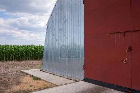 Photo for A large arched hangar sheathed with galvanized profiled sheet in the yard of the farm. Corn field nearby. Midsummer in the central region of Ukraine. - Royalty Free Image