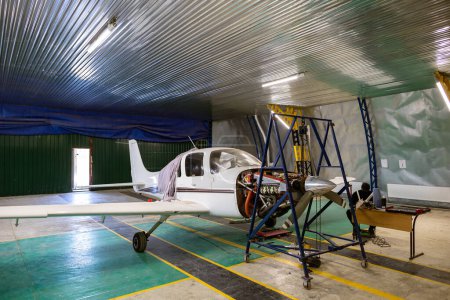 Foto de El hangar es un taller de reparación de automóviles para pequeñas empresas. Aviones monomotores ligeros, que necesitan reparación del motor. Un motor de avión está suspendido en un polipasto de cadena. - Imagen libre de derechos