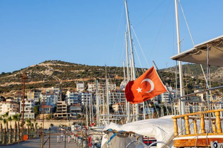 Red Turkish flag fluttering with sailboats in the background at a marina.
