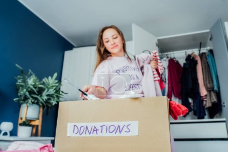 Photo for A cardboard box of selected clothes for donating to a Charity shop standing on the bed. Decluttering, Sorting clothes, and Cleaning Up. Reuse, second-hand. Conscious consumer, sustainability - Royalty Free Image