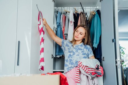 Woman selecting clothes from her wardrobe for donating to a Charity shop. Decluttering, Sorting clothes and Cleaning Up. Reuse, second-hand concept. Conscious consumer, sustainable lifestyle
