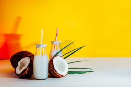 Photo for Bottles with coconut non-dairy milk drink and fresh coconuts on bright yellow background with color light. Trendy coctails. Healthy vegan plant base coconut milk. Selective focus. Copy space. - Royalty Free Image