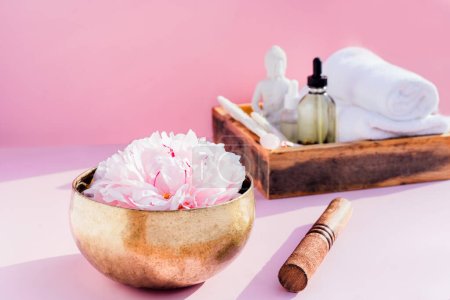 Tibetan singing bowl with floating peony flower and spa wellness exotic massage set on the pink background. Asian relaxing spa procedure with essential oils. Alternative medicine and body care