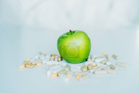Photo for Green apple in the pile of different pills on the white. Choose between natural, folk and traditional synthetic way of vitamins, health care. Diet modification, diabetes management, drugs alternative - Royalty Free Image