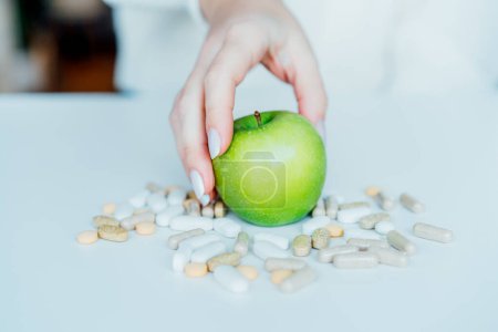 Photo for Female hand taking green apple from the pile of pills. Choose between natural, folk and traditional synthetic way of vitamins, health care. Diet modification, diabetes management, drugs alternative - Royalty Free Image