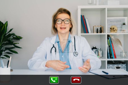 Foto de Imagen de la doctora de mediana edad hablando con el cliente en línea en la computadora, enfermera hablando con el paciente enfermo en una videollamada, usando un portátil. Concepto de telemedicina. Cita médica remota en línea. - Imagen libre de derechos