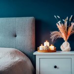 Autumn decor in stylish modern bedroom. Cozy interior with dark emerald wall, bed with grey fabric headboard, beige blanket, bedside table, vase with pampas grass, pumpkin and burning candles on tray