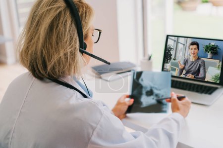 Arzt mittleren Alters in weißem Kittel und Videokonferenzkopfhörer machen Online-Videotelefonate mit dem Patienten am Laptop. Telemedizinisches Konzept für die häusliche Gesundheitsversorgung. Online-Fernarzttermin