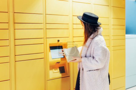 Photo for Fashion woman with box using modern postal automatic mail terminal with self service device for pickup or refund an order. Electronic locker for storing parcels. Online shopping. Selective focus - Royalty Free Image