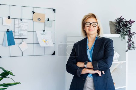 Photo for Smiling middle aged businesswoman near grid mood board with pinned work-life balance wheel diagram on her work space. Finding Balance in Your Life. Life planning. Coaching tools. Selective focus. - Royalty Free Image