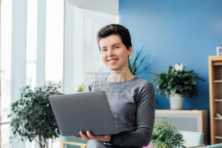 Porträt einer lächelnden Frau mittleren Alters mittleren Alters in lässigem Outfit, die im modernen Büro, Besprechungsraum und Konferenzraum am Laptop arbeitet. Organisation von Geschäftsprozessen. Bequemer Arbeitsplatz