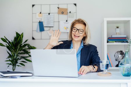Mujer de negocios madura sonriente teniendo videoconferencia, entrevistando en línea en el ordenador portátil en la oficina, confiado de mediana edad experimentado profesional senior, CEO de la empresa. Empresaria.