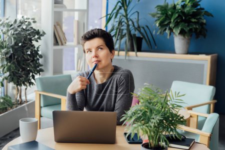 Middle aged minded pensive employee business woman in casual clothes holds a pen, works at office desk with pc laptop. Achievement career concept. Dreaming, planning, Taking time for recovery