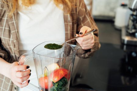 Close up woman adding spirulina or chlorella powder during making smoothie on the kitchen. Superfood supplement. Healthy detox vegan diet. Healthy dieting eating, weight loss program. Selective focus.
