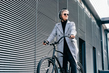 Homme élégant en manteau, lunettes de soleil et casque de protection sur vélo rétro près du mur urbain gris. Transport neutre de l'empreinte carbone. Mobilité écologique verte transport durable