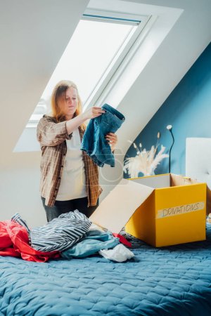 Woman selecting clothes from her wardrobe for recycling, donating to a Charity shop. Decluttering, Sorting clothes, Cleaning Up. Reuse, second hand concept. Conscious consumer, sustainable lifestyle