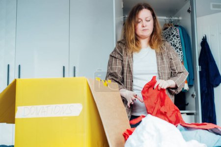 Mujer seleccionando ropa de su armario para su reciclaje, donando a una tienda de caridad. Decluttering, clasificación de ropa, limpieza. Reutilización, concepto de segunda mano. Consumidor consciente, estilo de vida sostenible