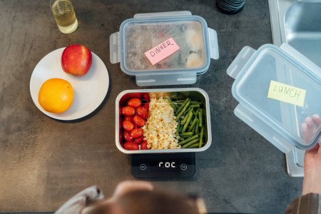 Téléchargez les photos : Healthy diet plan for weight loss, daily ready meal menu. Close up Woman weighing lunch box cooked in advance,ready to eat on kitchen scale. Balanced portion with healthy dish. Pre-cooking concept. - en image libre de droit