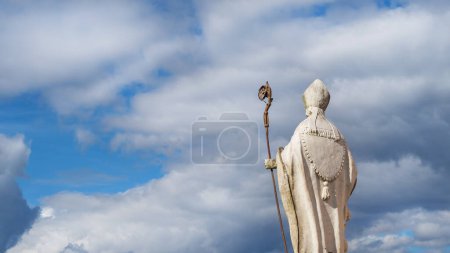 Religión cristiana y espiritualidad. Obispo o Papa estatua antigua con crosier y mitra contra el cielo celestial