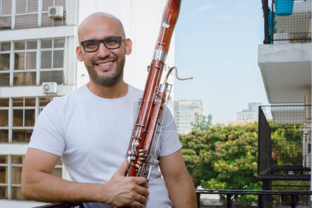 portrait of young Venezuelan musician of the Simon Bolivar symphony orchestra, at home holding a bassoon, standing on the balcony smiling and looking at the camera.
