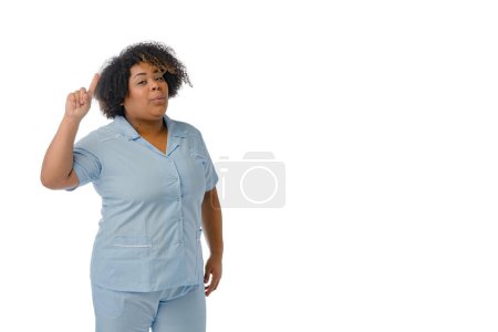 Foto de Joven afro mujer latina médico en uniforme azul está de pie con el dedo hacia arriba y tiene una idea, fondo blanco con espacio para copiar - Imagen libre de derechos