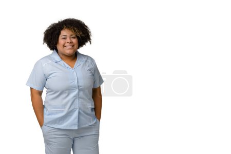 Foto de Retrato de una joven afro-latina médica de etnia venezolana, en uniforme azul posando, sonriendo y mirando a la cámara, fondo blanco - espacio para copiar, concepto de medicina. - Imagen libre de derechos