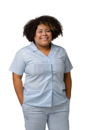 Foto de Retrato vertical de cintura hacia arriba de una joven venezolana afro latina en uniforme azul, pelo afro, de pie sonriendo y mirando a la cámara feliz. Fondo blanco - Imagen libre de derechos