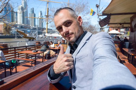Téléchargez les photos : Homme d'affaires caucasien d'origine française, souriant joyeusement en vacances en Argentine, au restaurant à Puerto Madero assis en train de prendre des photos selfie avec son téléphone - en image libre de droit