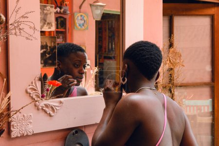 Rückansicht einer jungen Afrofrau haitianischer Herkunft, mit kurzen Haaren, die zu Hause steht und sich im Spiegel anstarrt